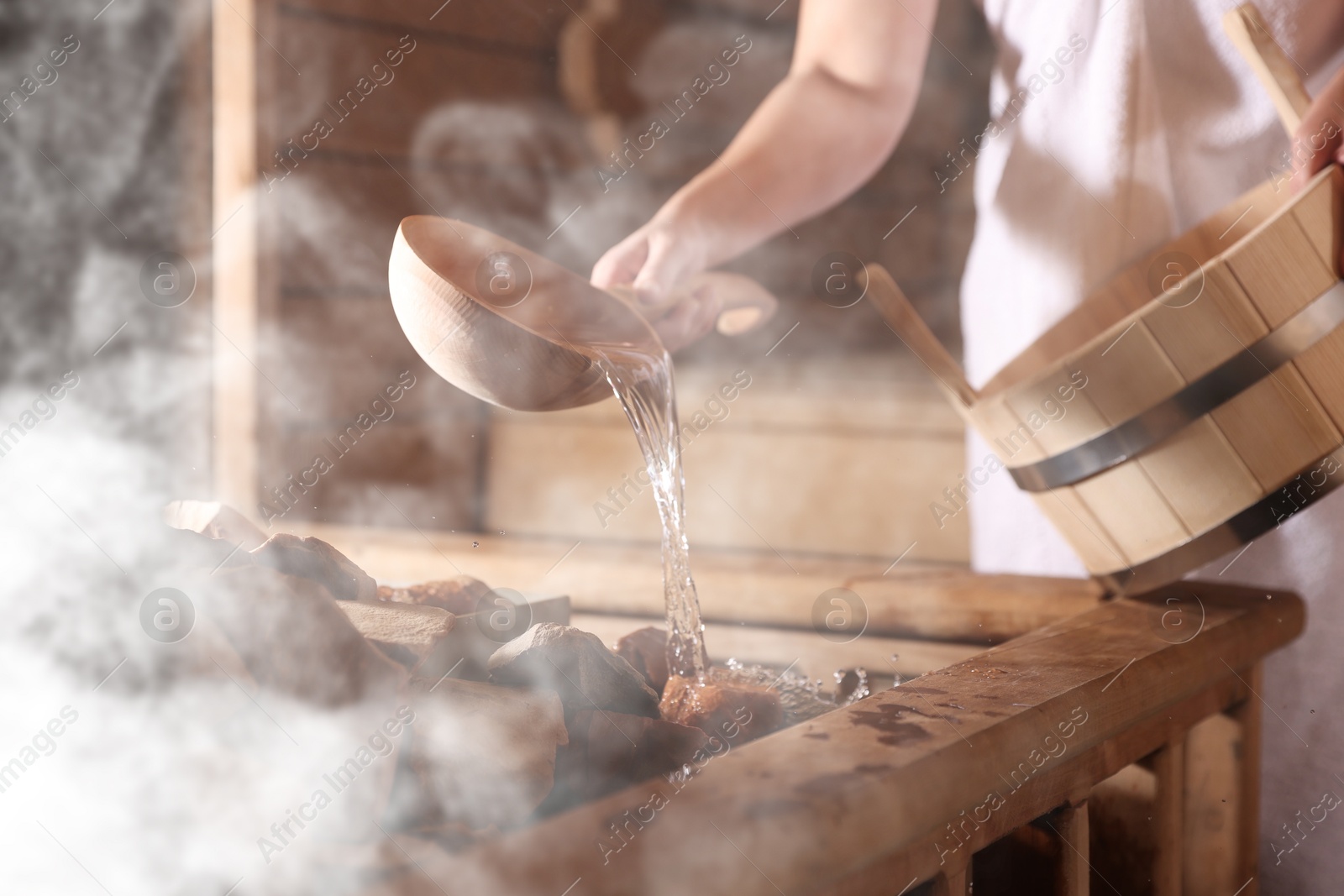 Woman pouring water onto stones surrounded by steam in sauna, closeup Image of Woman pouring water onto stones surrounded by steam in sauna, closeup