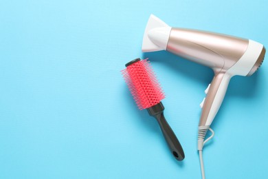 Photo of Hair dryer and brush on light blue background, top view. Space for text