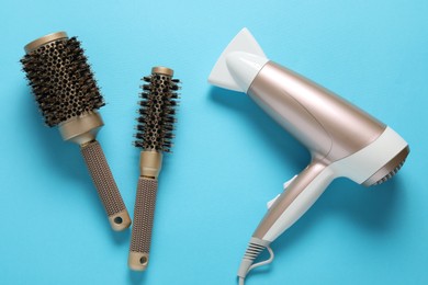 Photo of Hair dryer and brushes on light blue background, flat lay