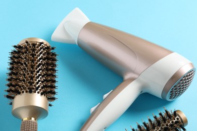 Photo of Hair dryer and brushes on light blue background, closeup