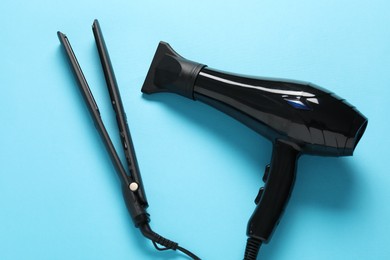 Photo of Hair dryer and straightener on light blue background, top view