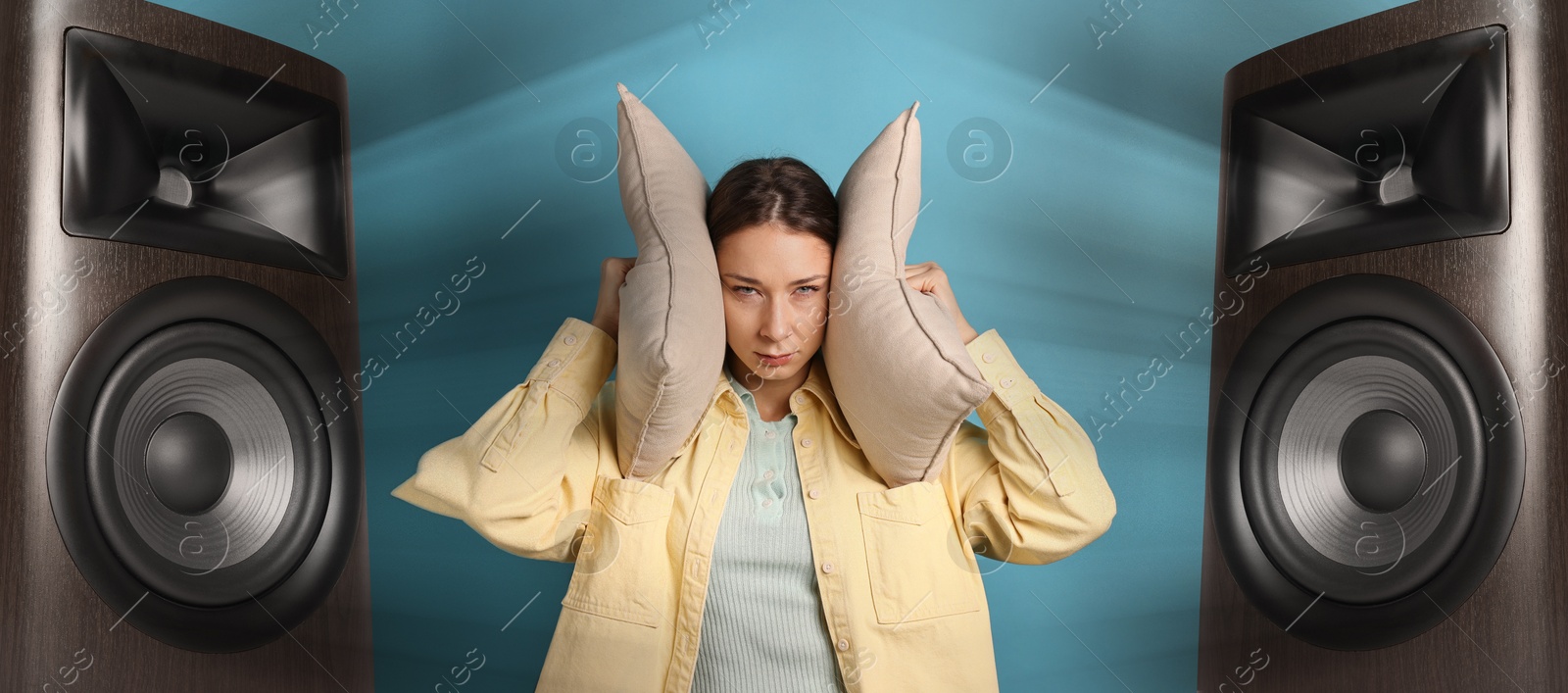 Annoyed woman covering her ears with pillows from loud sound of audio speakers on blue background Image of Annoyed woman covering her ears with pillows from loud sound of audio speakers on blue background