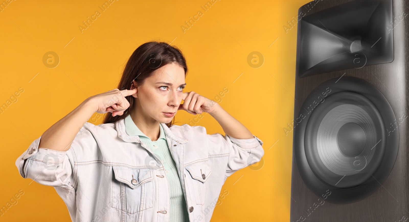 Annoyed woman covering her ears from loud sound of audio speaker on orange background Image of Annoyed woman covering her ears from loud sound of audio speaker on orange background