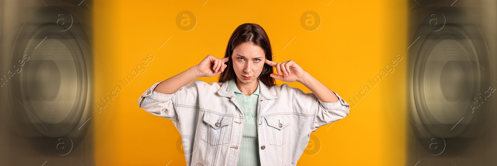 Annoyed woman covering her ears from loud sound of audio speakers on orange background Image of Annoyed woman covering her ears from loud sound of audio speakers on orange background