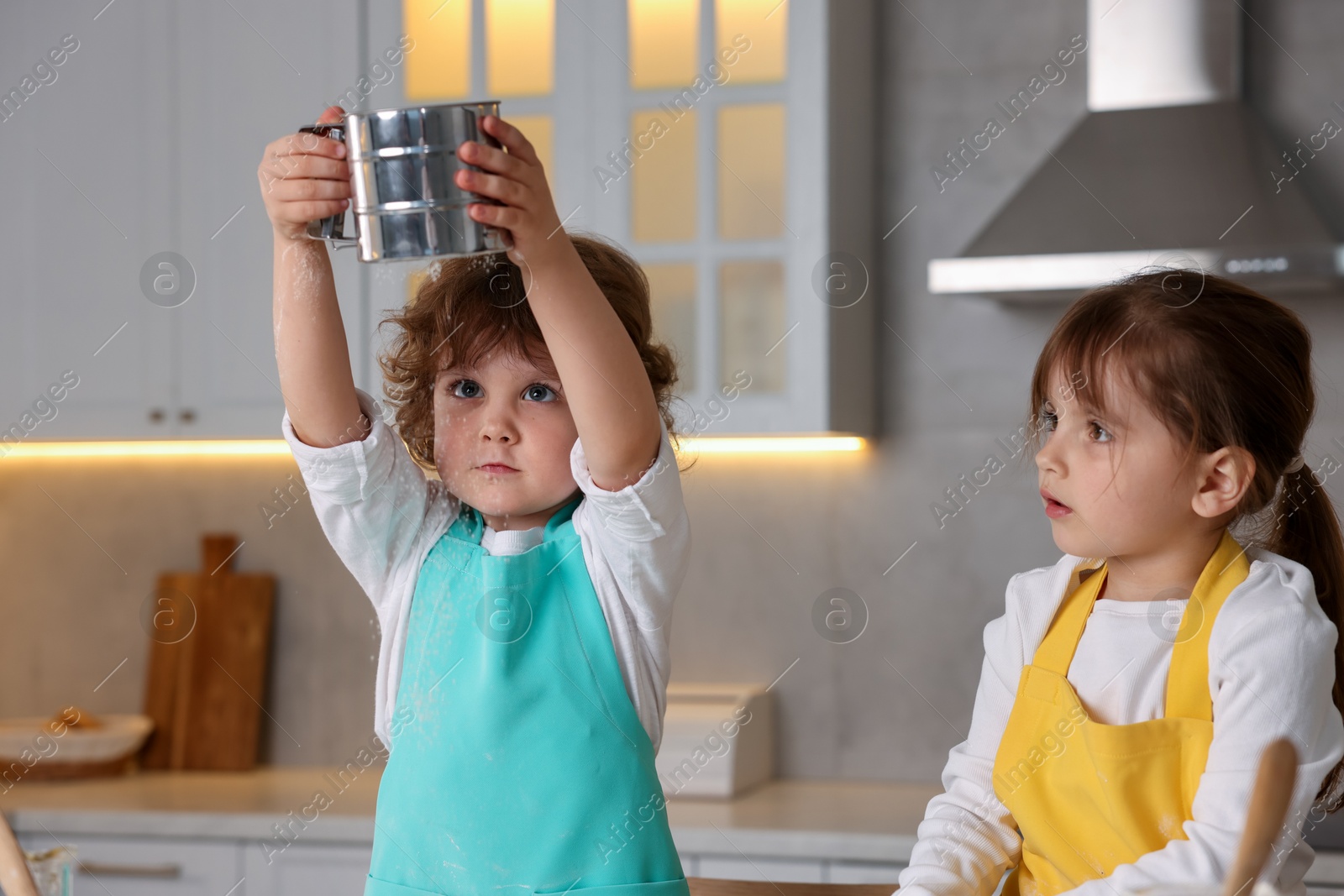 Cooking recipe. Cute children sieving flour at table in kitchen Photo of Cooking recipe. Cute children sieving flour at table in kitchen