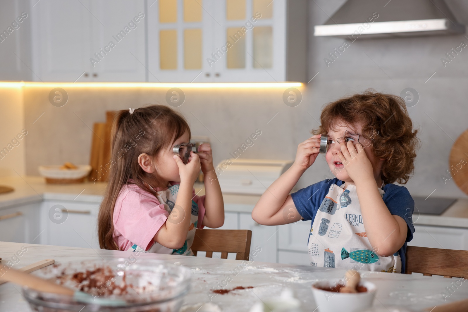 Cooking recipe. Little children with cookie cutters at table in kitchen Photo of Cooking recipe. Little children with cookie cutters at table in kitchen