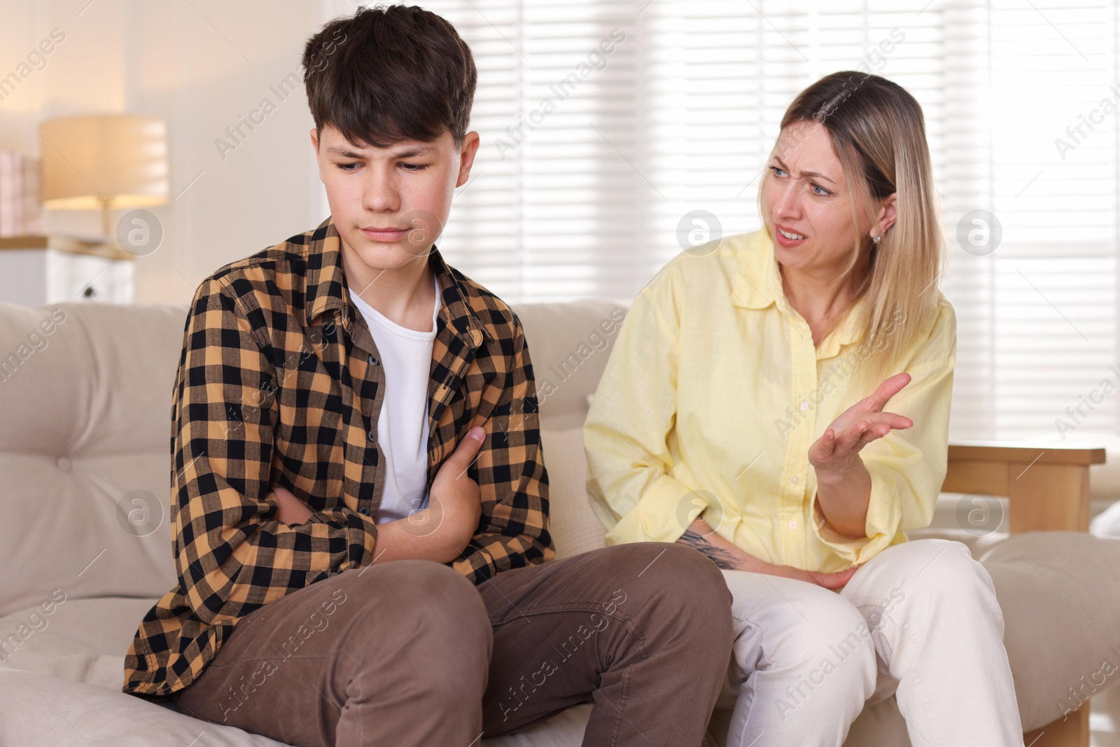 Mother scolding her teenage son on sofa at home Photo of Mother scolding her teenage son on sofa at home