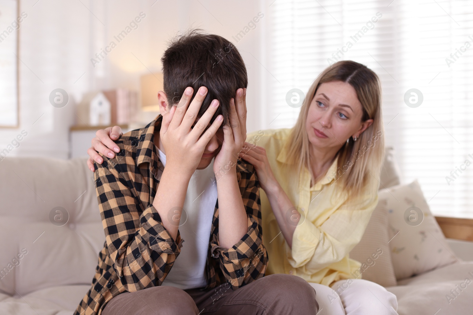 Mother consoling her upset son on sofa at home Photo of Mother consoling her upset son on sofa at home