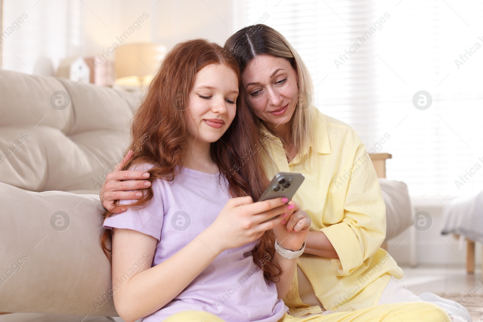 Mother and her daughter watching something on smartphone at home Photo of Mother and her daughter watching something on smartphone at home