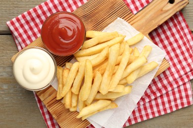 Photo of Tasty french fries with sauces on wooden table, top view