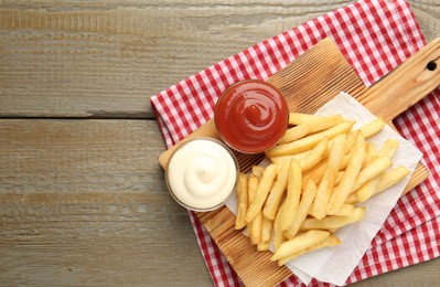 Photo of Tasty french fries with sauces on wooden table, top view. Space for text