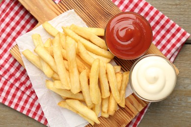 Photo of Tasty french fries with sauces on wooden table, top view