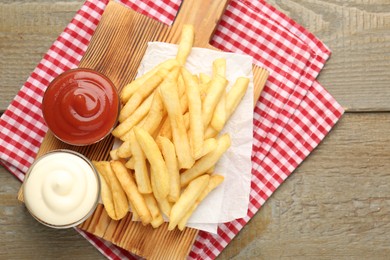 Photo of Tasty french fries with sauces on wooden table, top view