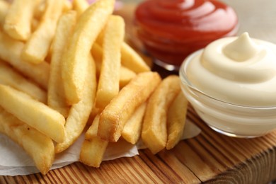 Photo of Tasty french fries with sauces on wooden table, closeup