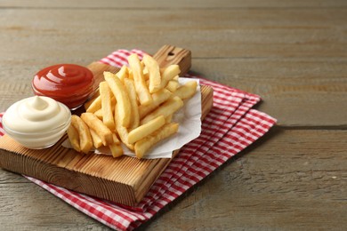 Photo of Tasty french fries with sauces on wooden table. Space for text