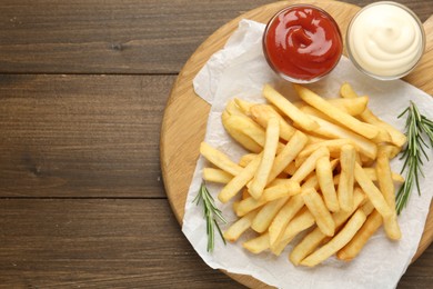 Photo of Tasty french fries with sauces and rosemary on wooden table, top view. Space for text