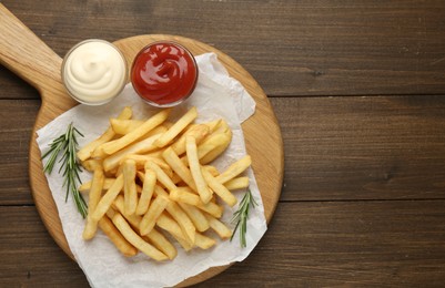 Photo of Tasty french fries with sauces and rosemary on wooden table, top view. Space for text