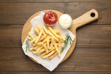 Photo of Tasty french fries with sauces and rosemary on wooden table, top view