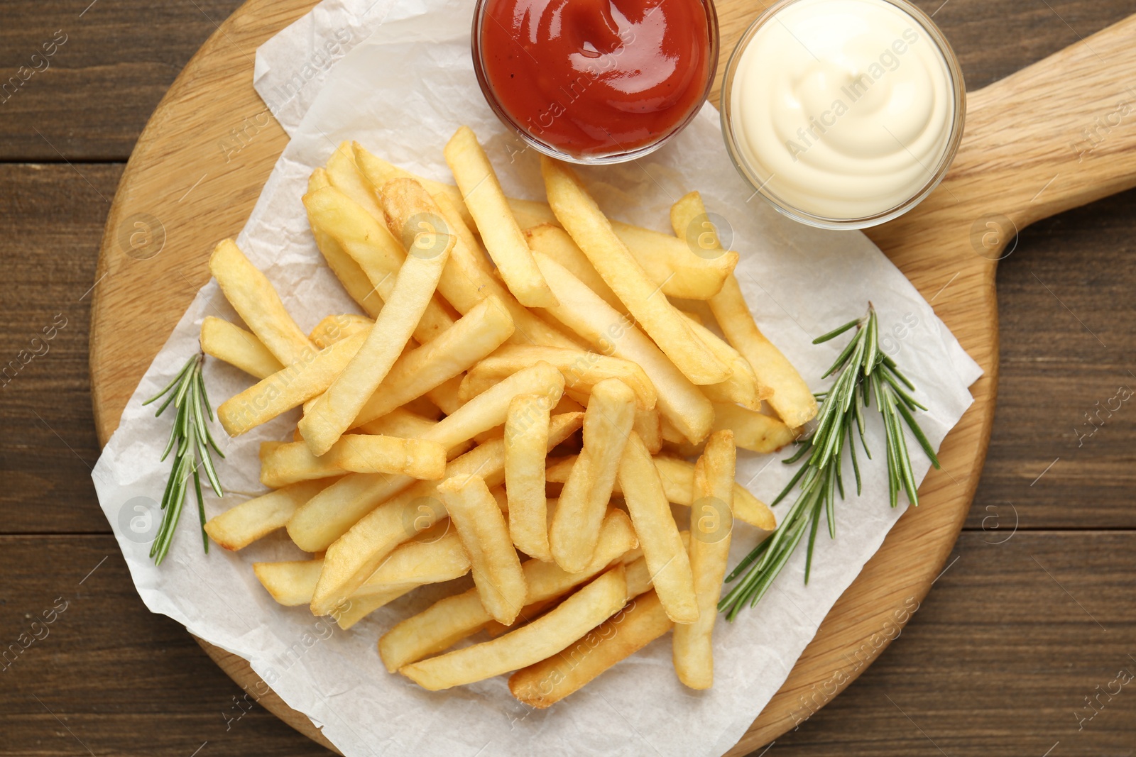 Photo of Tasty french fries with sauces and rosemary on wooden table, top view