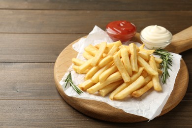Photo of Tasty french fries with sauces and rosemary on wooden table, closeup. Space for text