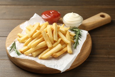 Photo of Tasty french fries with ketchup and rosemary on wooden table, closeup
