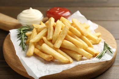 Photo of Tasty french fries with ketchup and rosemary on wooden table, closeup