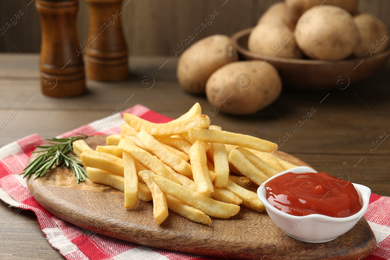 Photo of Tasty french fries with ketchup and rosemary on wooden table, closeup