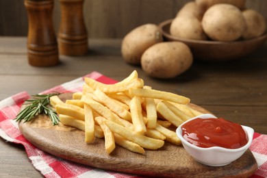 Photo of Tasty french fries with ketchup and rosemary on wooden table, closeup