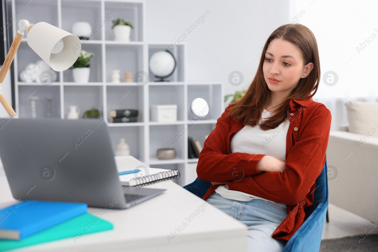 Teenage girl doing homework with laptop at table indoors Photo of Teenage girl doing homework with laptop at table indoors
