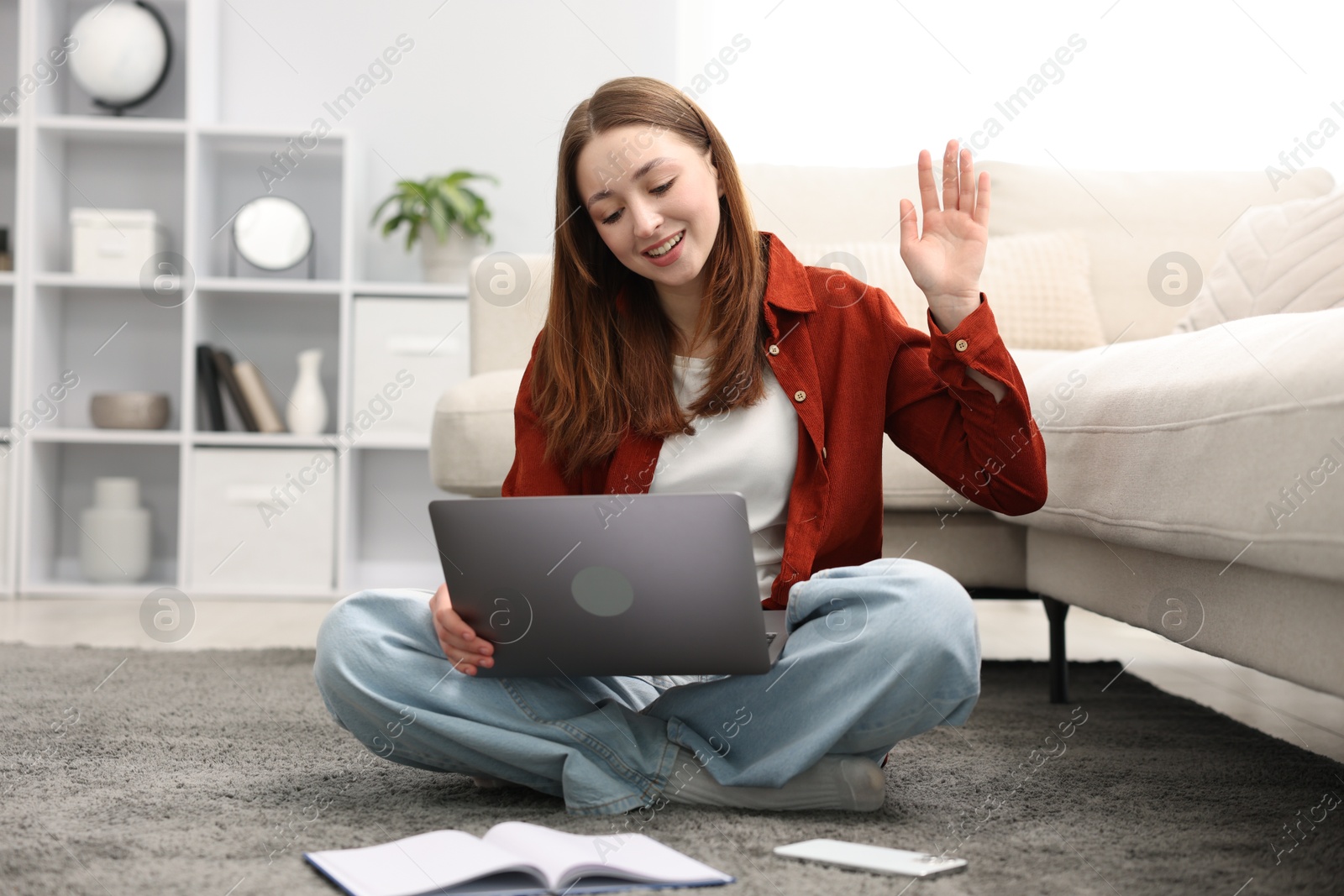 Photo of Teenage girl having video chat via laptop on floor at home