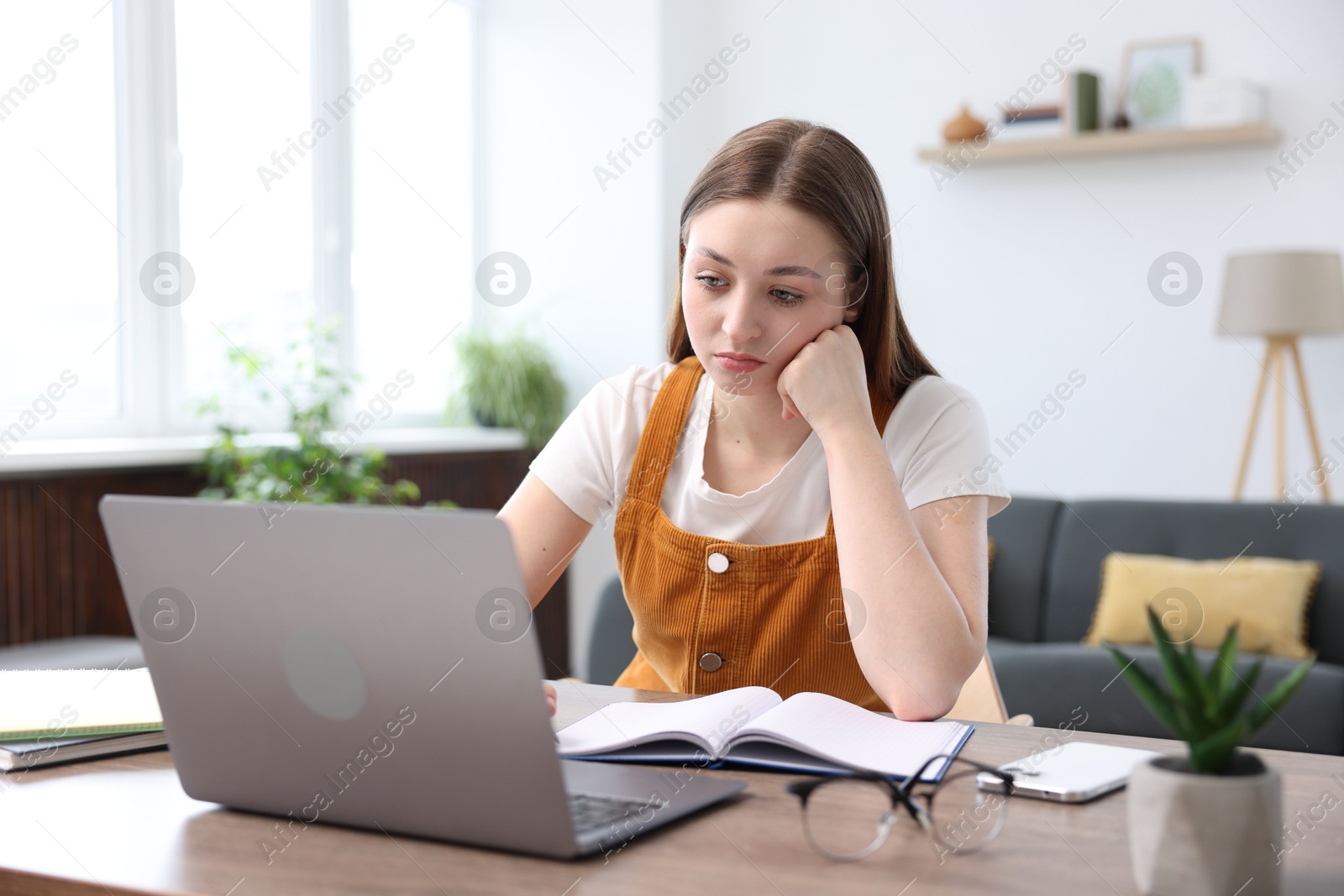 Teenage girl doing homework with laptop at table indoors Photo of Teenage girl doing homework with laptop at table indoors