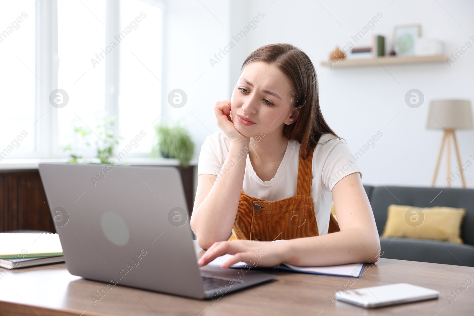 Teenage girl doing homework with laptop at table indoors Photo of Teenage girl doing homework with laptop at table indoors
