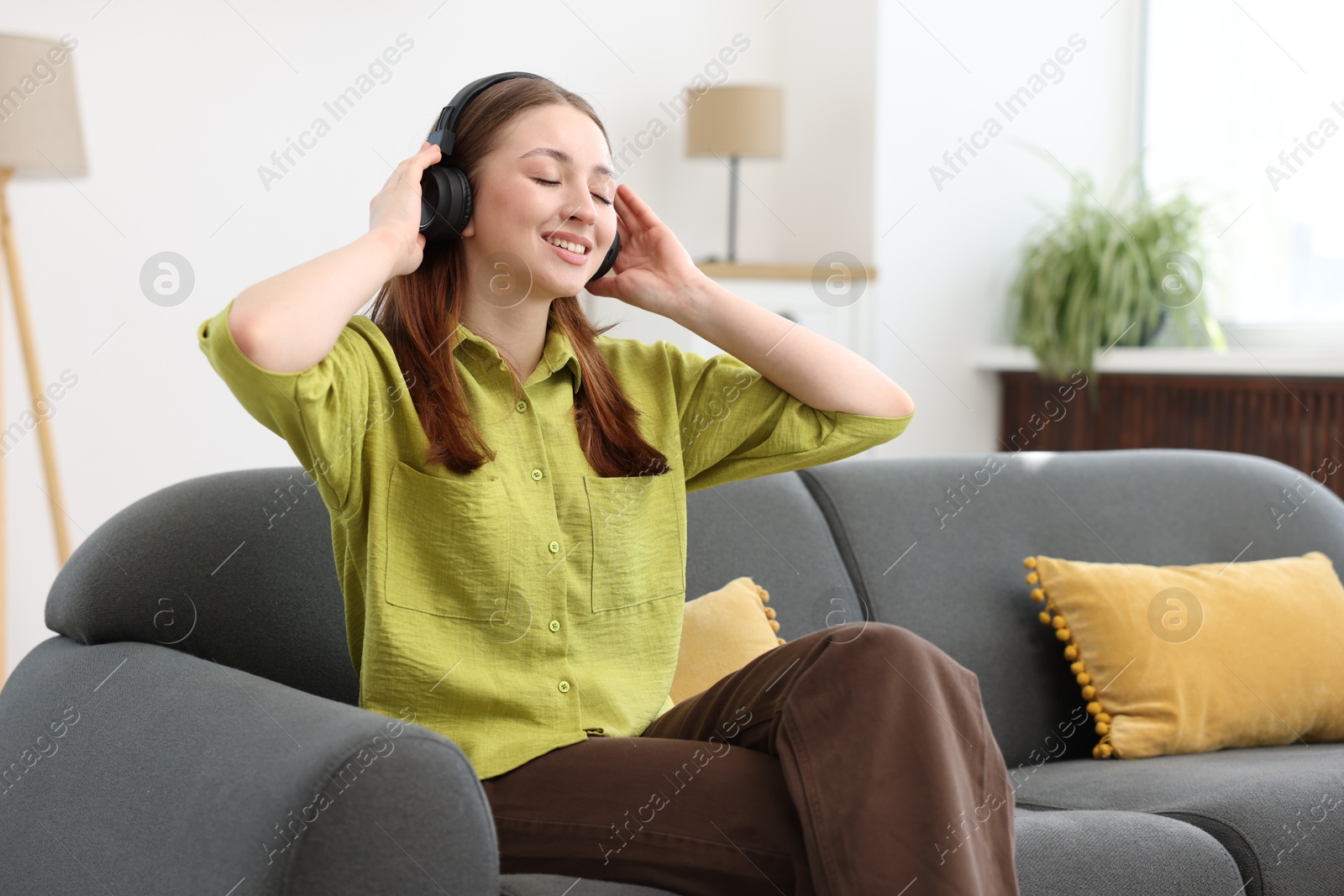 Teenage girl in headphones listening to music on sofa at home Photo of Teenage girl in headphones listening to music on sofa at home