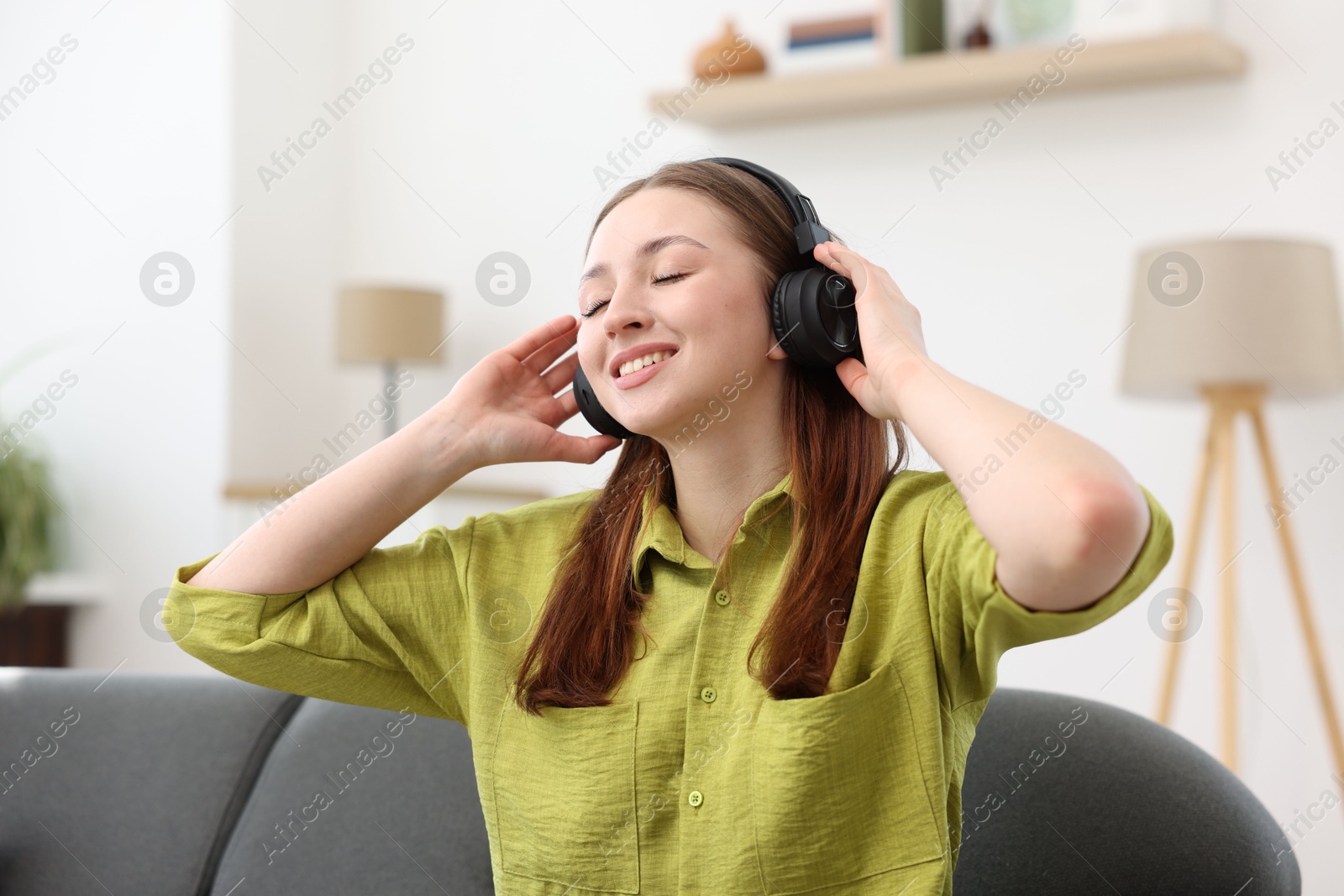 Teenage girl in headphones listening to music on sofa at home Photo of Teenage girl in headphones listening to music on sofa at home