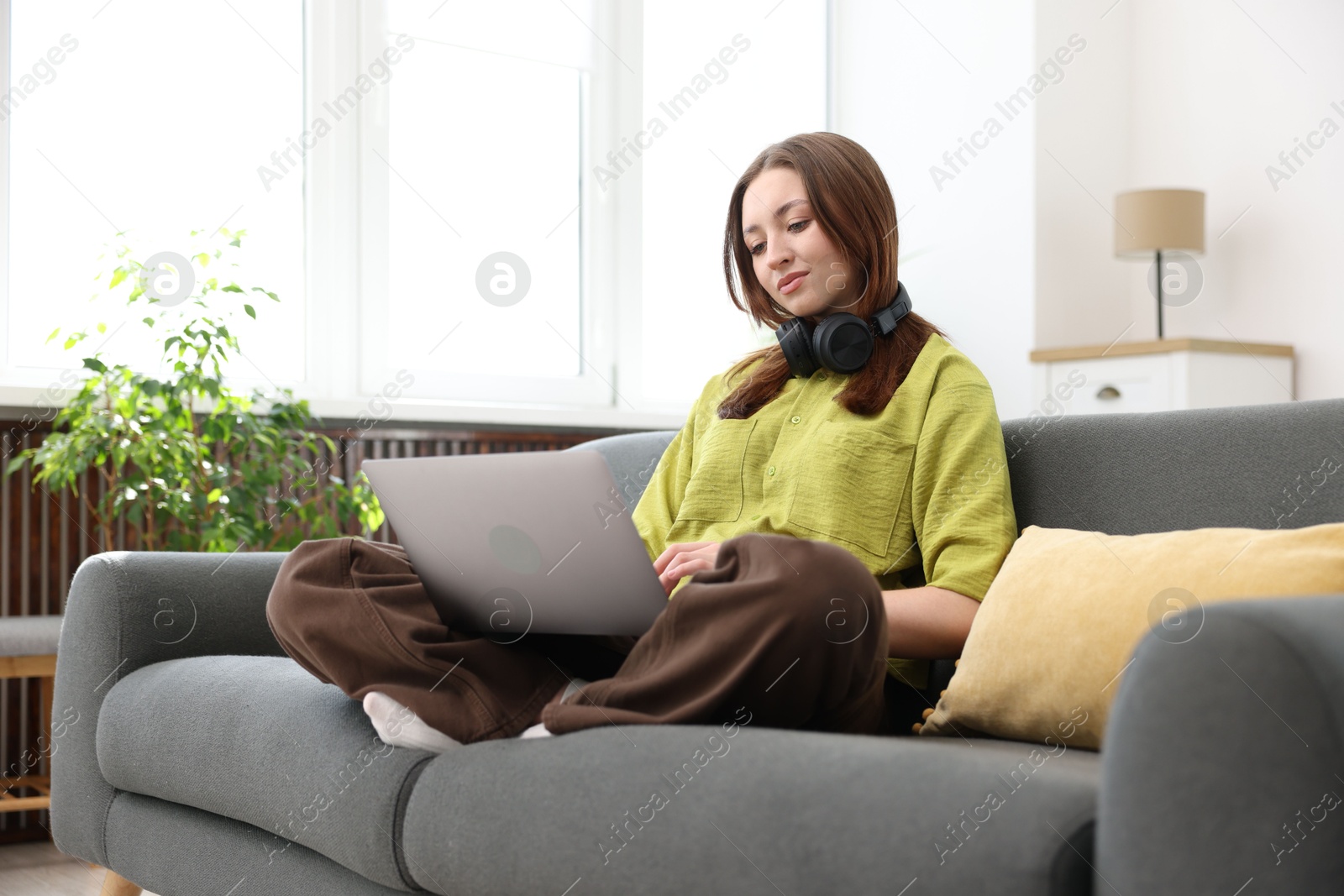 Teenage girl with headphones using laptop on sofa at home Photo of Teenage girl with headphones using laptop on sofa at home