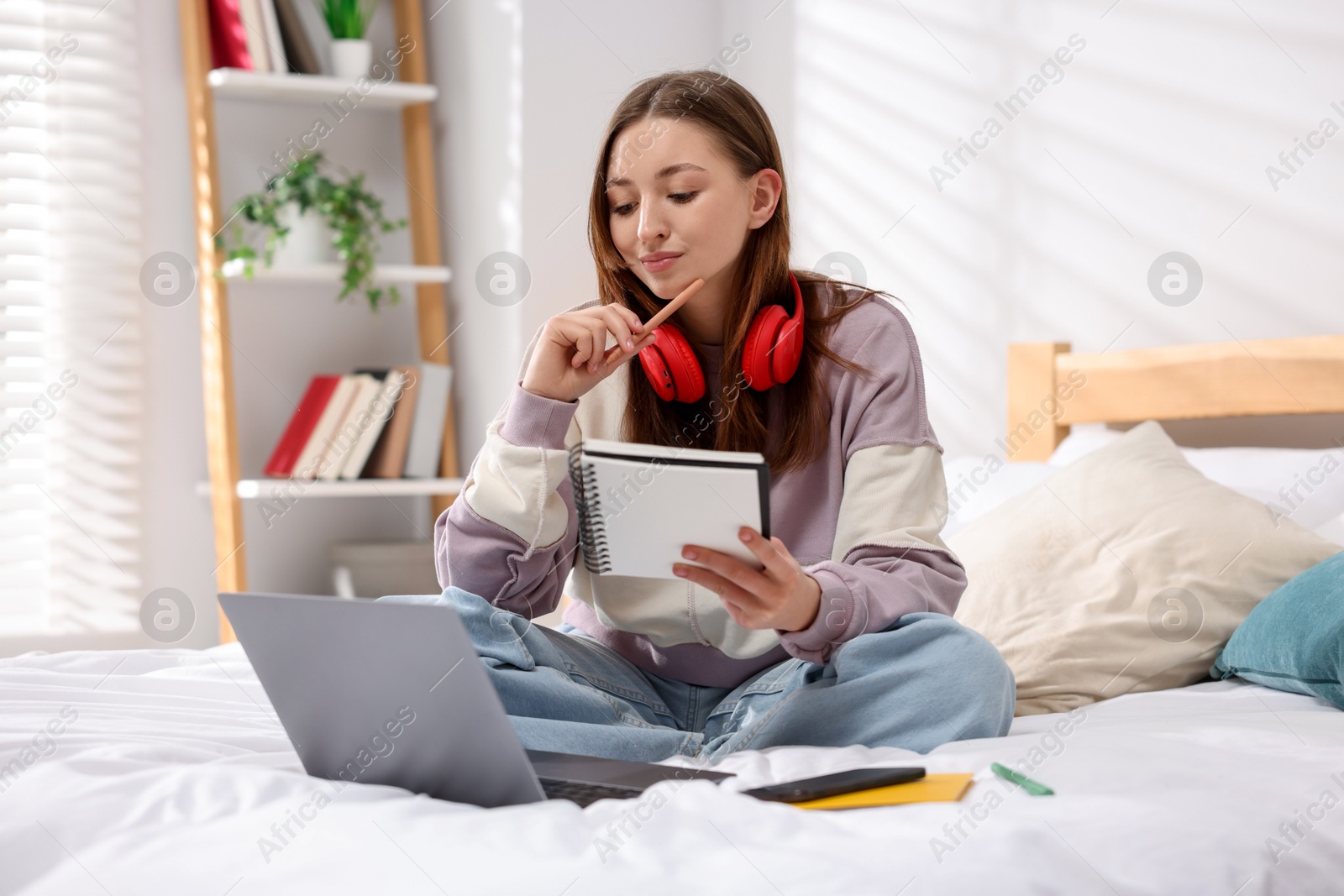 Teenage girl doing homework near laptop on bed at home Photo of Teenage girl doing homework near laptop on bed at home