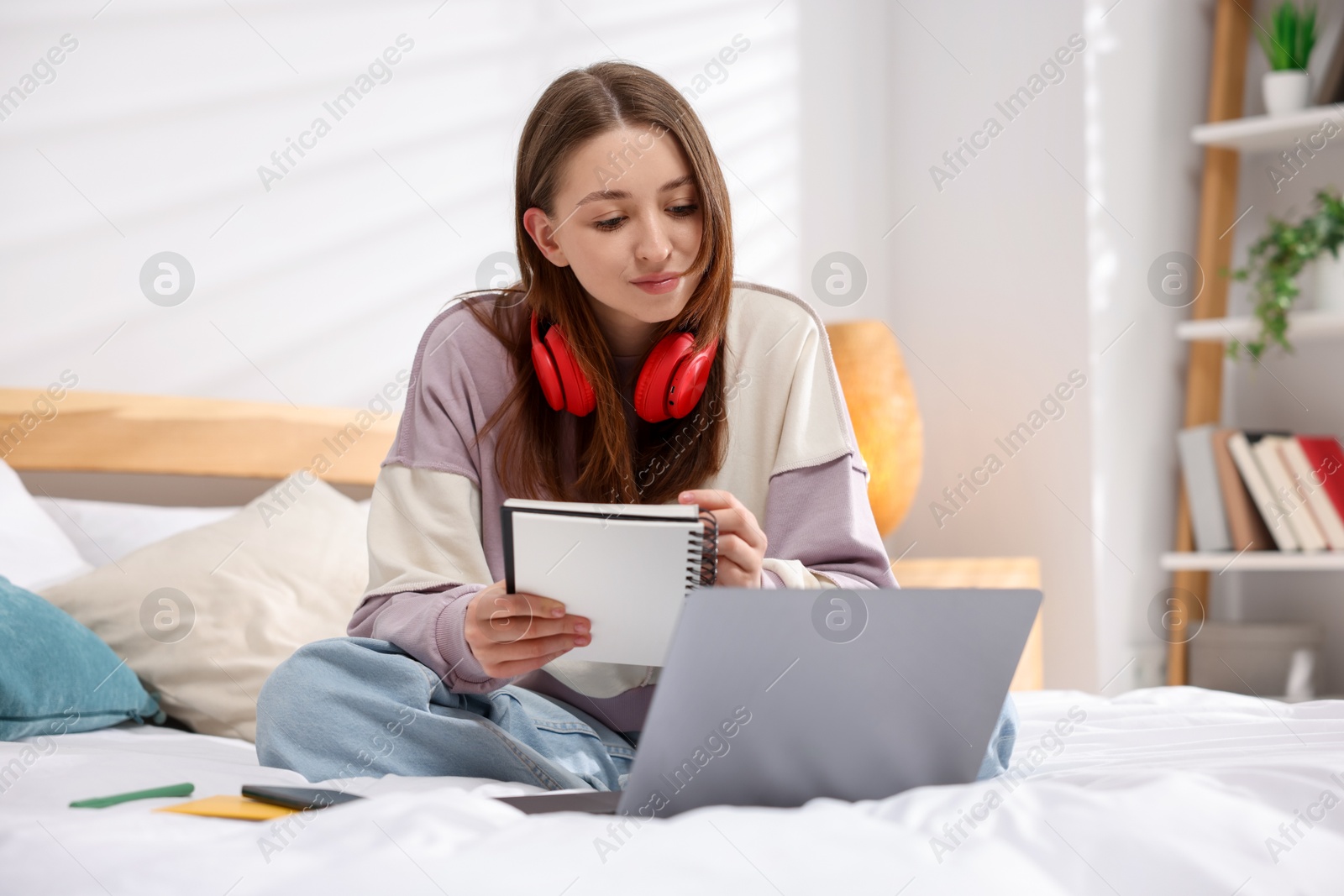 Teenage girl doing homework near laptop on bed at home Photo of Teenage girl doing homework near laptop on bed at home