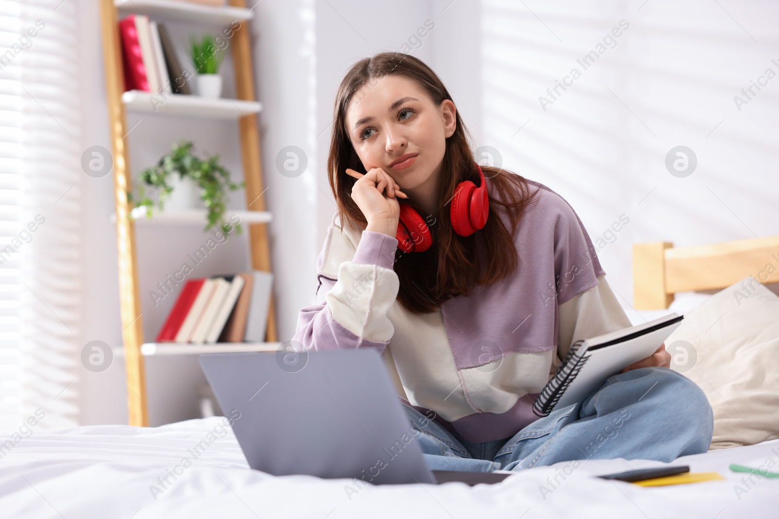 Teenage girl doing homework near laptop on bed at home Photo of Teenage girl doing homework near laptop on bed at home