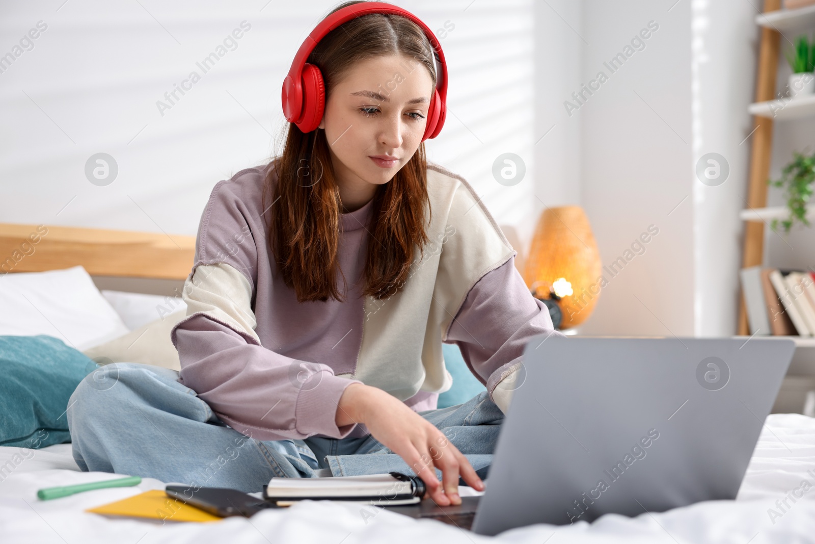 Teenage girl in headphones using laptop on bed at home Photo of Teenage girl in headphones using laptop on bed at home