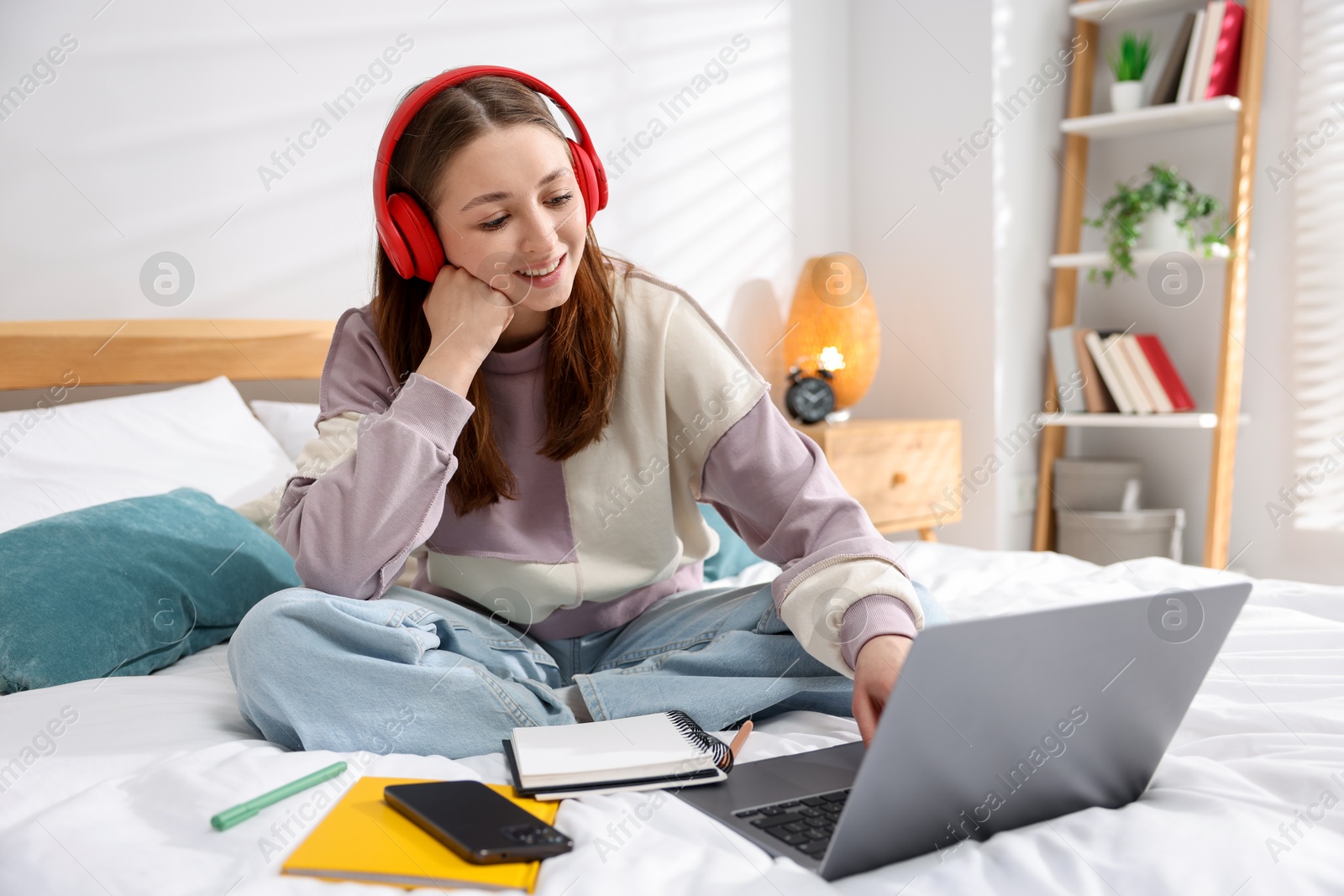 Teenage girl in headphones using laptop on bed at home Photo of Teenage girl in headphones using laptop on bed at home