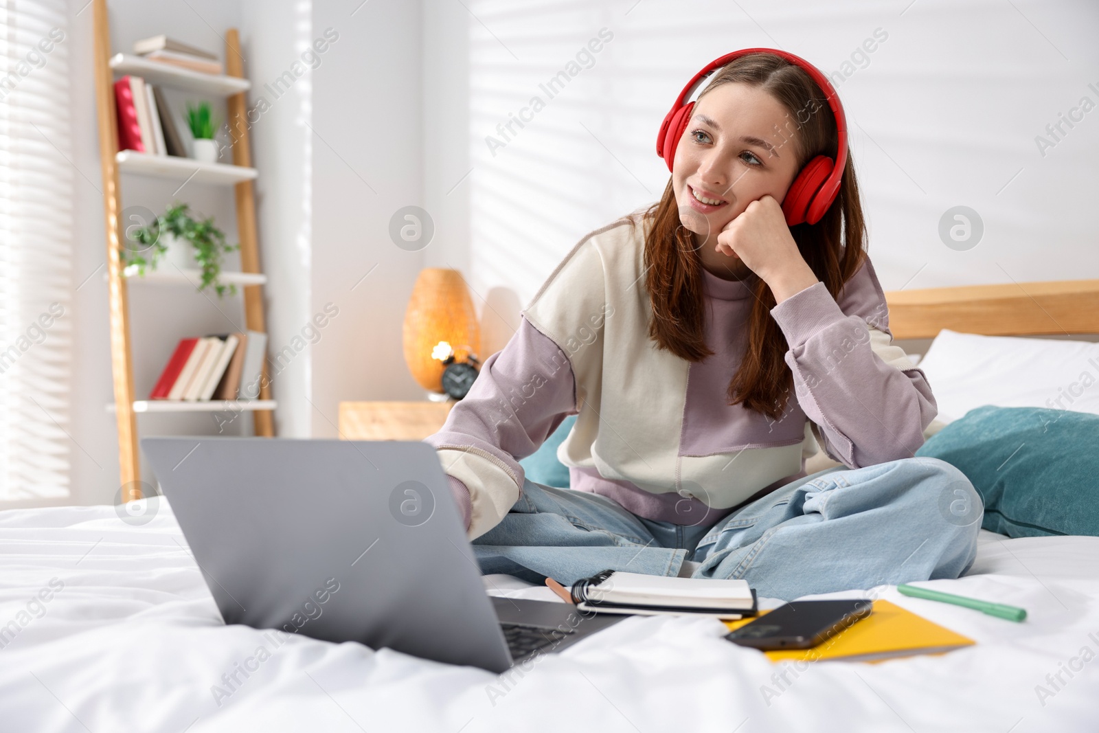 Photo of Teenage girl in headphones using laptop on bed at home