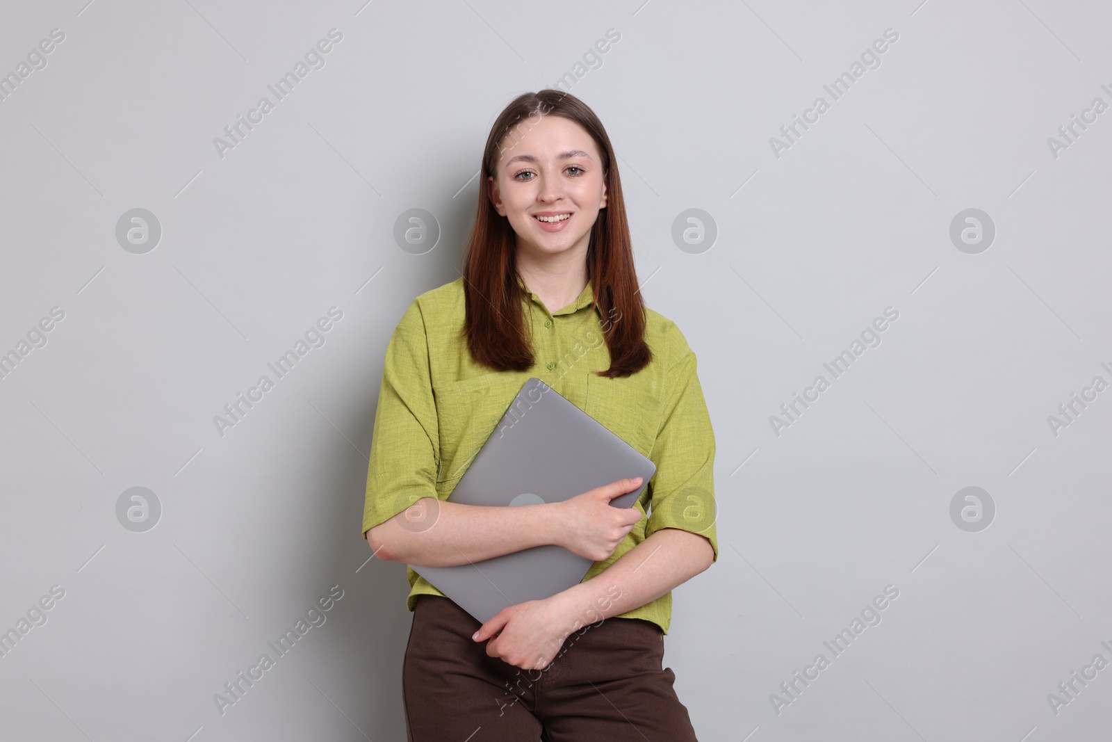 Happy teenage girl with laptop on light grey background Photo of Happy teenage girl with laptop on light grey background