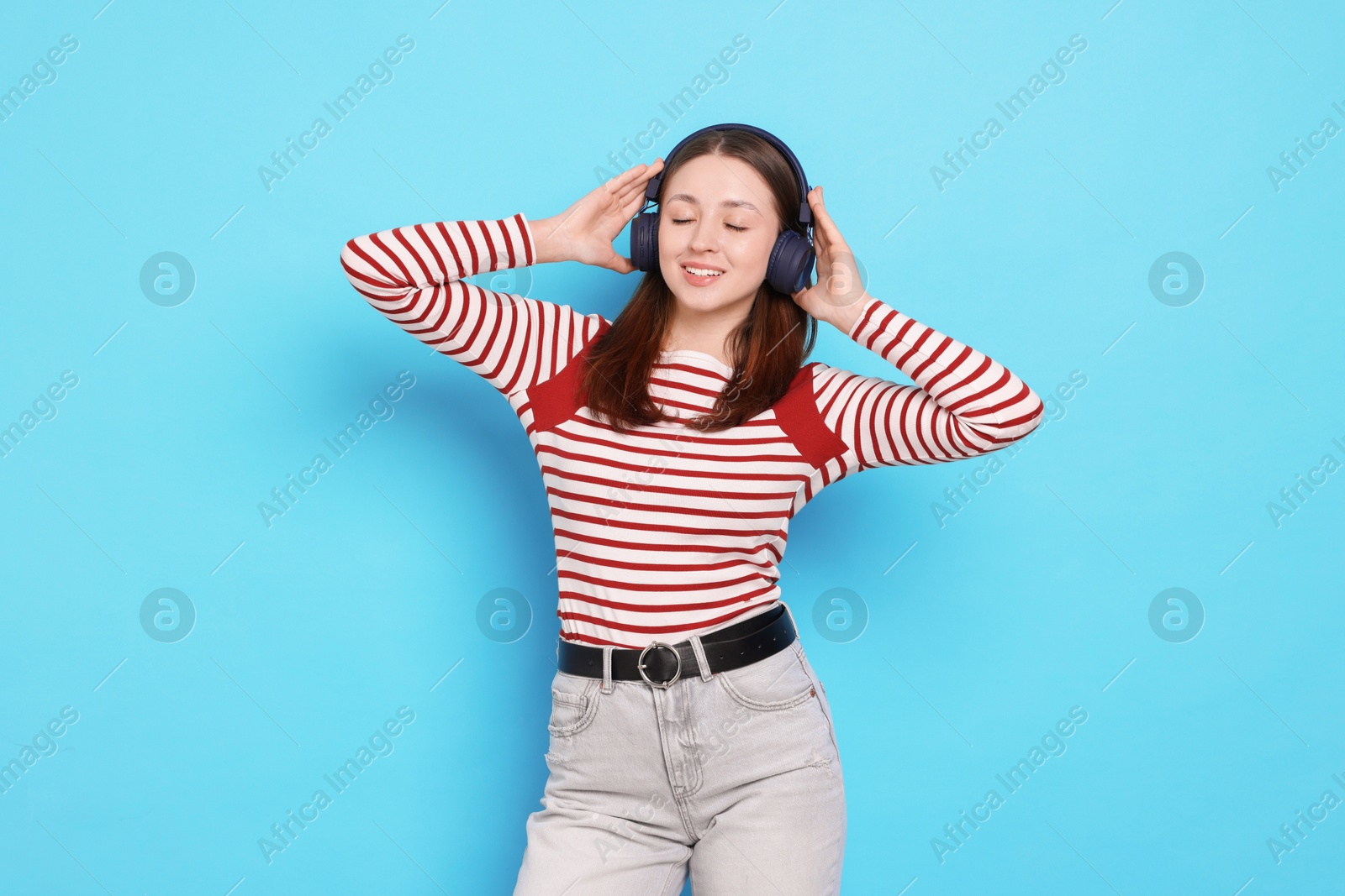 Teenage girl in headphones on light blue background Photo of Teenage girl in headphones on light blue background