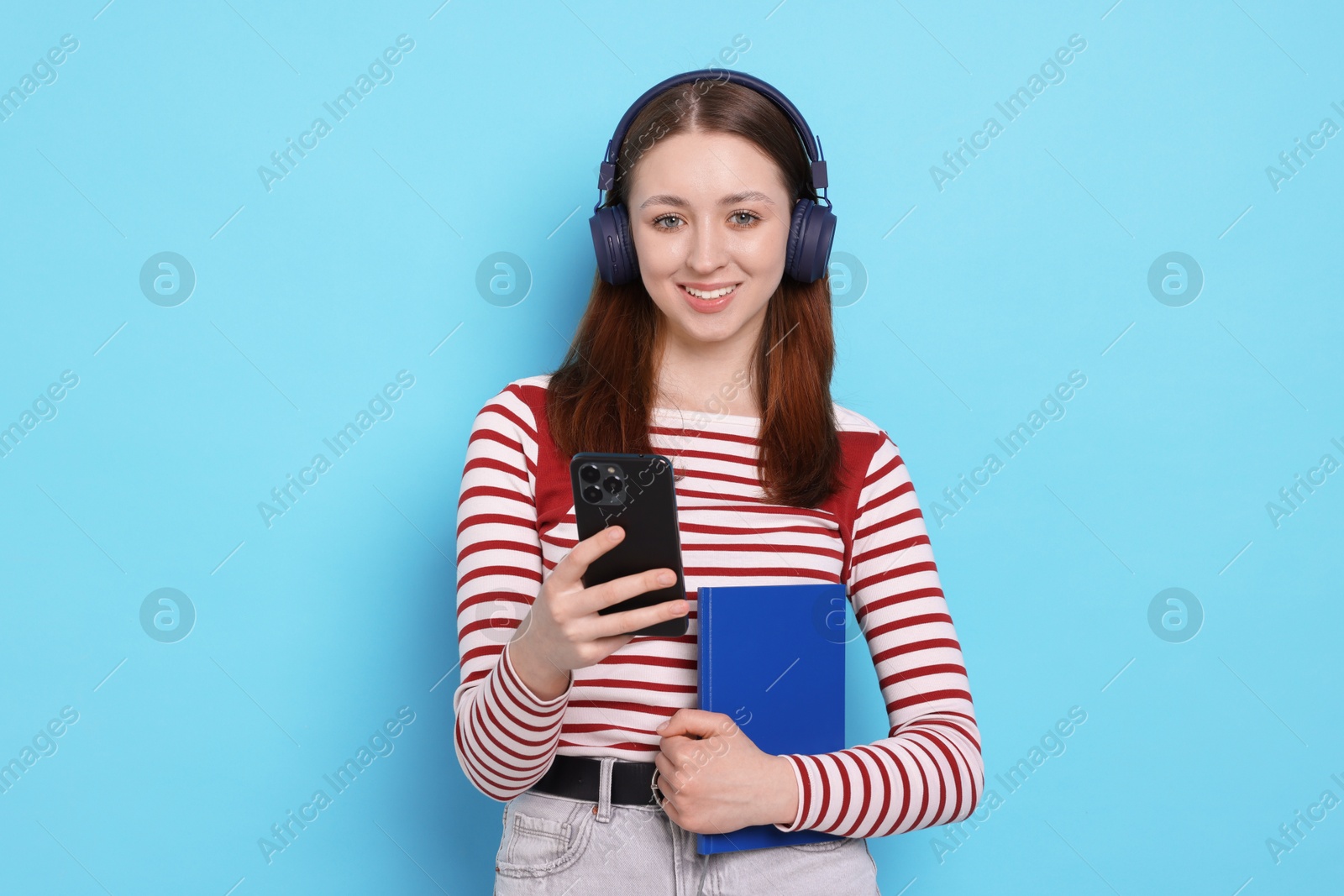 Photo of Teenage girl in headphones with smartphone and notebook on light blue background