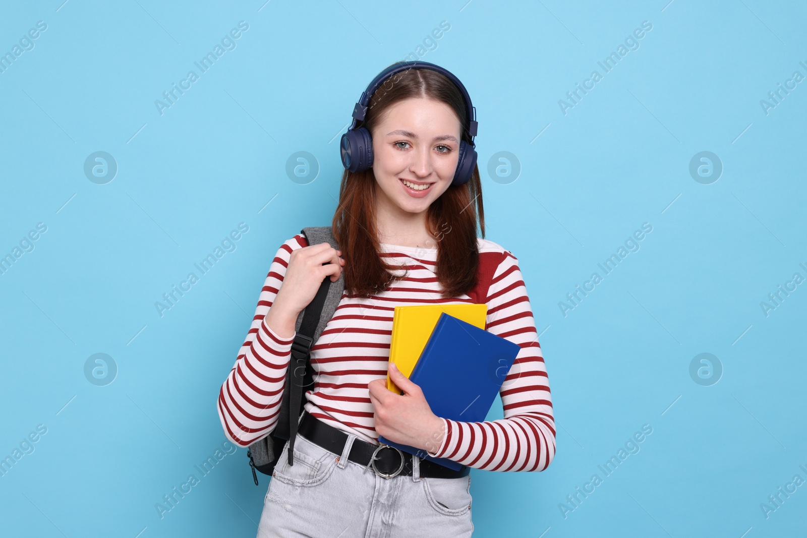 Teenage girl in headphones with backpack and notebooks on light blue background Photo of Teenage girl in headphones with backpack and notebooks on light blue background