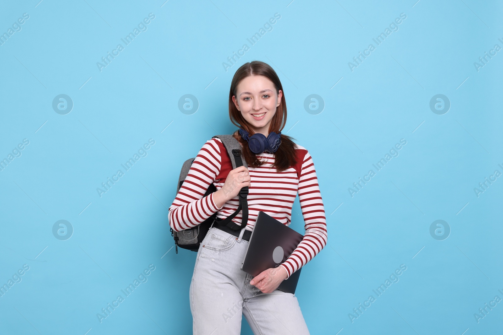 Teenage girl with headphones, backpack and laptop on light blue background Photo of Teenage girl with headphones, backpack and laptop on light blue background