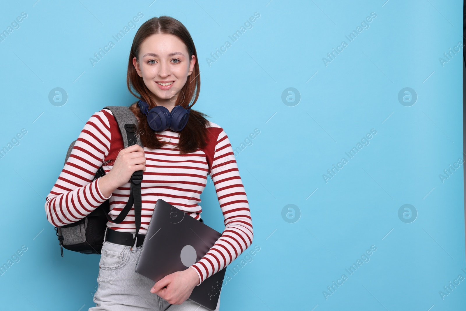 Photo of Teenage girl with headphones, backpack and laptop on light blue background, space for text