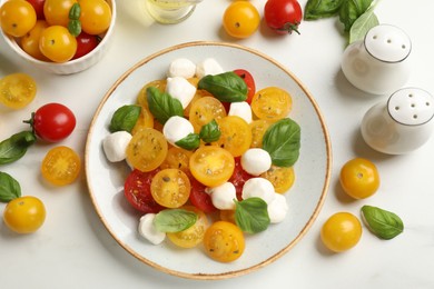 Photo of Fresh salad with yellow tomatoes, basil and mozzarella cheese on white marble table, flat lay