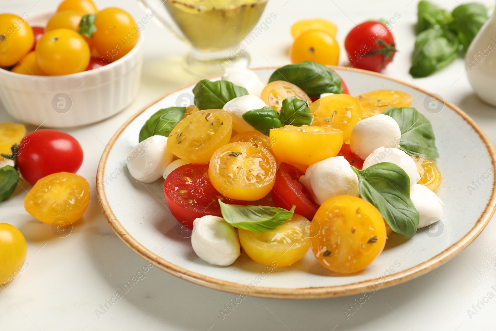 Fresh salad with yellow tomatoes, basil and mozzarella cheese on white marble table, closeup Photo of Fresh salad with yellow tomatoes, basil and mozzarella cheese on white marble table, closeup