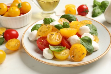 Photo of Fresh salad with yellow tomatoes, basil and mozzarella cheese on white marble table, closeup